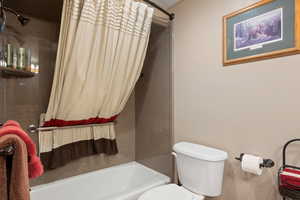 Full bathroom featuring toilet and shower / bath combination with curtain