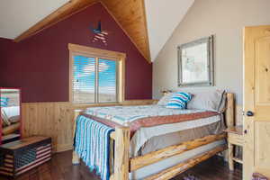 Bedroom with hardwood / wood-floors, wooden walls, wainscoting, and vaulted ceiling