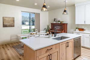 Kitchen with stainless steel dishwasher, an island with sink, light wood-type flooring, light countertops, and a sink