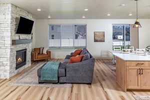 Living room with light wood finished floors, baseboards, a stone fireplace, and recessed lighting