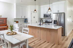 Kitchen with tasteful backsplash, a sink, appliances with stainless steel finishes, light wood-style floors, and white cabinetry