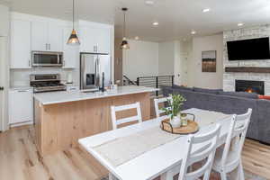 Kitchen featuring light wood-type flooring, white cabinetry, appliances with stainless steel finishes, open floor plan, and a center island with sink