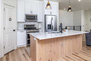 Kitchen featuring light wood-style flooring, appliances with stainless steel finishes, an island with sink, and white cabinets