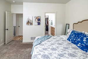 Carpeted bedroom with a walk in closet, baseboards, visible vents, and connected bathroom