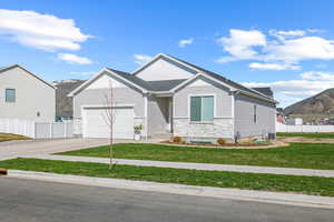 View of front of property with stone siding, fence, a front lawn, an attached garage, and driveway