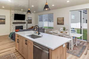 Kitchen featuring stainless steel dishwasher, light brown cabinetry, a sink, open floor plan, and light wood finished floors