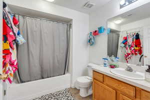 Full bathroom with toilet, shower / bathtub combination with curtain, vanity, and visible vents