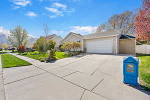 View of front of property with an attached garage, concrete driveway, fence, and a front lawn