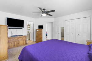 Bedroom with light colored carpet, a closet, ceiling fan, and ensuite bath