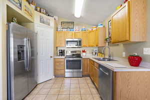 Kitchen featuring light tile patterned floors, a sink, light countertops, stainless steel appliances, and lofted ceiling