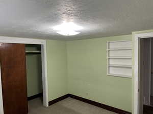 Unfurnished bedroom featuring a textured ceiling, a closet, baseboards, and carpet