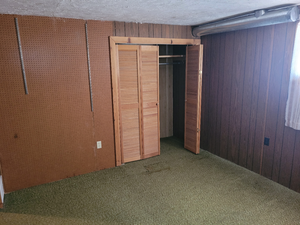 Unfurnished bedroom with a textured ceiling, a closet, wood walls, and carpet floors