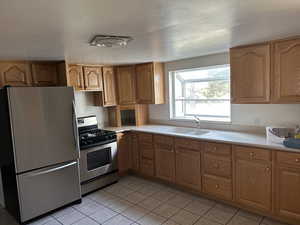 Kitchen with a sink, light countertops, light tile patterned flooring, and stainless steel appliances