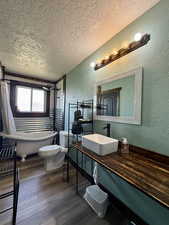 Full bath featuring a textured wall, a textured ceiling, a soaking tub, toilet, and wood finished floors