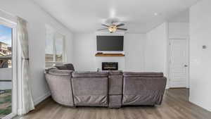 Living area with a ceiling fan, wood finished floors, baseboards, and a glass covered fireplace