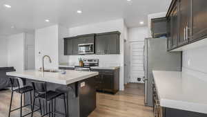 Kitchen with light countertops, a kitchen bar, appliances with stainless steel finishes, light wood finished floors, and a sink