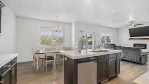 Kitchen featuring light countertops, stainless steel dishwasher, ceiling fan with notable chandelier, a sink, and wood finished floors