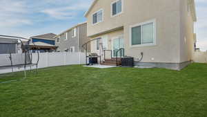 Back of house with a trampoline, stucco siding, central AC unit, a fenced backyard, and a lawn