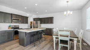 Kitchen with a sink, appliances with stainless steel finishes, a notable chandelier, and light wood finished floors
