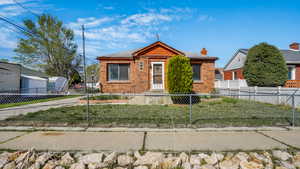Bungalow-style home with brick siding, a front lawn, and a fenced front yard