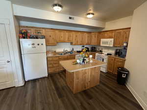 Kitchen featuring visible vents, a sink, dark wood-style flooring, and white appliances