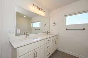 Primary Bathroom with tile patterned floors, double vanity, a sink, and baseboards