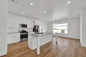 Kitchen featuring an island with sink, white cabinets,  appliances with stainless steel finishes, and a large sink
