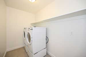 Washroom with independent washer and dryer, light tile patterned flooring, laundry area, and baseboards