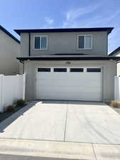 View of front facade with a garage, stucco siding, fence, and concrete driveway