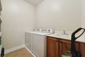 Laundry room featuring light tile patterned floors, baseboards, a sink, independent washer and dryer, and cabinet space