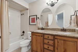 Full bathroom with a sink, toilet, shower / bathtub combination with curtain, and double vanity