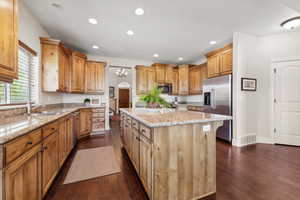 Kitchen featuring visible vents, a sink, stainless steel appliances, a kitchen island, and light stone counters