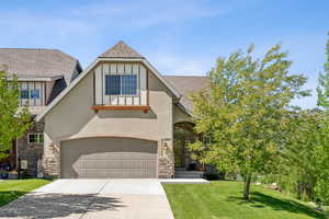 English style home with concrete driveway, stucco siding, stone siding, a front lawn, and a shingled roof