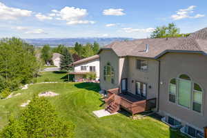 Back of property featuring roof with shingles, a deck with mountain view, a lawn, and stucco siding