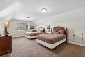 Bedroom featuring a textured ceiling, carpet flooring, baseboards, and lofted ceiling