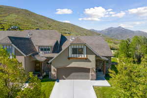 View of front facade featuring a mountain view, stone siding, driveway, and stucco siding