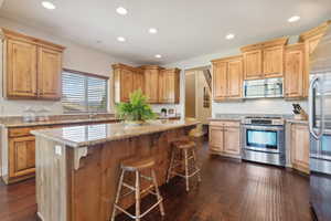 Kitchen with a kitchen breakfast bar, recessed lighting, a center island, appliances with stainless steel finishes, and dark wood-style flooring