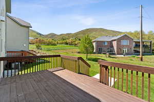 Wooden deck featuring a rural view, a mountain view, and a lawn
