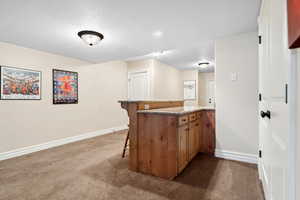 Kitchen featuring carpet flooring, a kitchen breakfast bar, baseboards, and brown cabinets