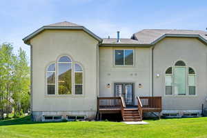 Rear view of property featuring roof with shingles, stucco siding, french doors, a wooden deck, and a lawn