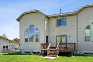 Back of property featuring roof with shingles, a deck, a lawn, and stucco siding