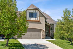 Tudor house with stucco siding, stone siding, an attached garage, a shingled roof, and concrete driveway