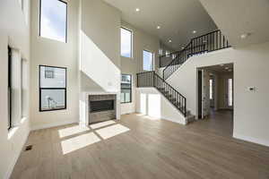 Unfurnished living room featuring a fireplace with flush hearth, recessed lighting, a high ceiling, light wood finished floors, and stairway