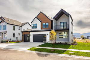 Modern farmhouse with a balcony, concrete driveway, a front lawn, an attached garage, and a mountain view