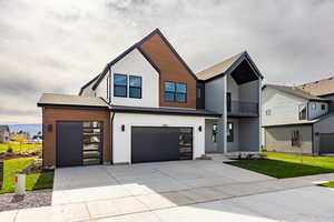 Contemporary house featuring concrete driveway, a balcony, a shingled roof, an attached garage, and a front yard