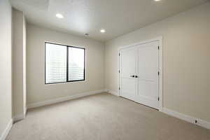 Unfurnished bedroom featuring light colored carpet, recessed lighting, a textured ceiling, and a closet