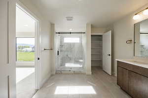 Bathroom with a marble finish shower, vanity, a textured ceiling, light tile patterned flooring, and a spacious closet