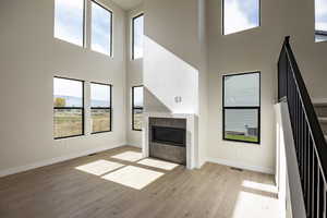 Unfurnished living room with a towering ceiling, a tiled fireplace, light wood finished floors, and stairway