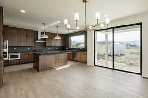 Kitchen featuring pendant lighting, a textured ceiling, decorative backsplash, a chandelier, and light wood-type flooring