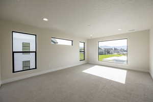 Empty room with light colored carpet, a textured ceiling, and recessed lighting